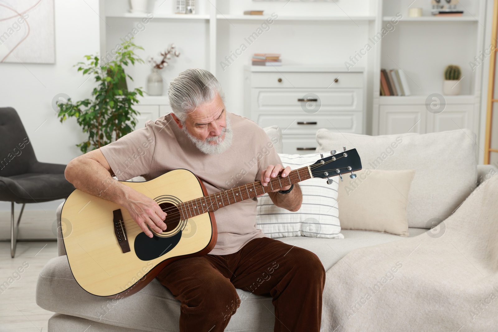 Photo of Relaxing hobby. Senior man playing guitar on sofa at home