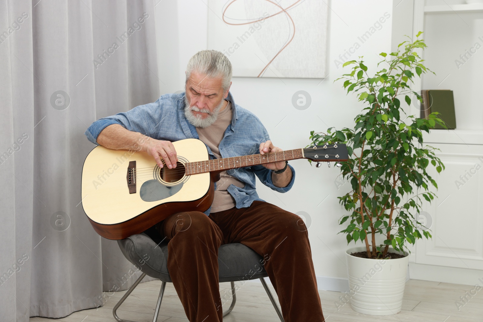 Photo of Relaxing hobby. Senior man playing guitar in armchair at home