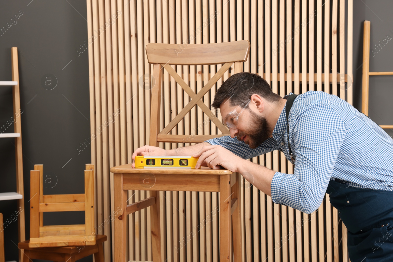 Photo of Relaxing hobby. Man using level tool while repairing wooden chair in workshop