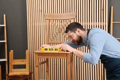 Photo of Relaxing hobby. Man using level tool while repairing wooden chair in workshop