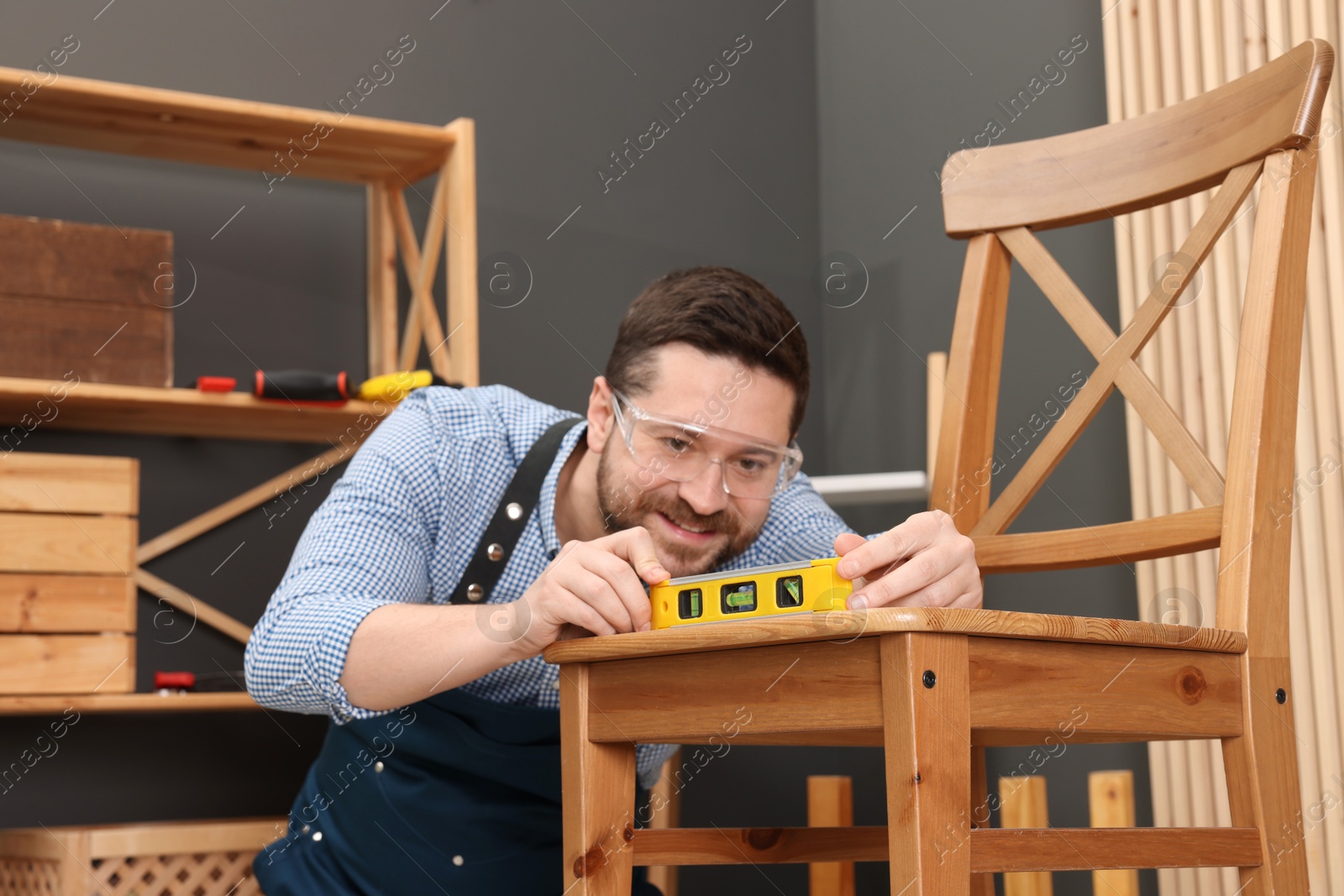 Photo of Relaxing hobby. Smiling man using level tool while repairing wooden chair in workshop