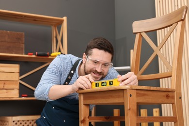 Relaxing hobby. Smiling man using level tool while repairing wooden chair in workshop