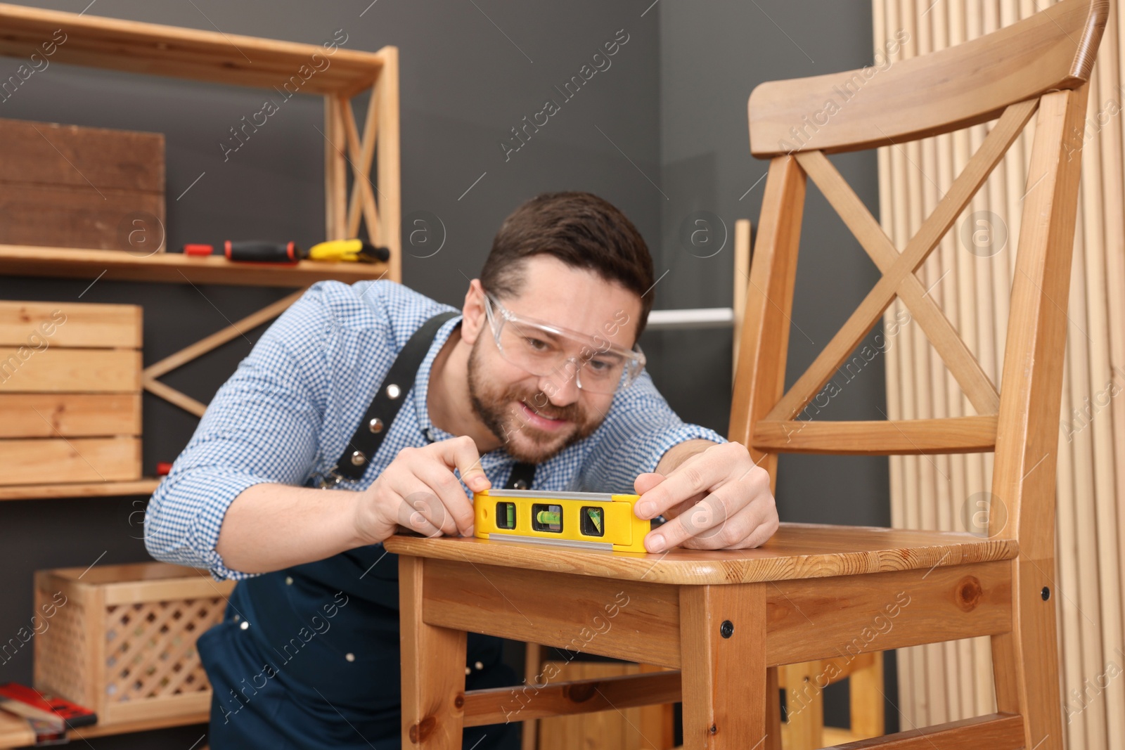 Photo of Relaxing hobby. Smiling man using level tool while repairing wooden chair in workshop