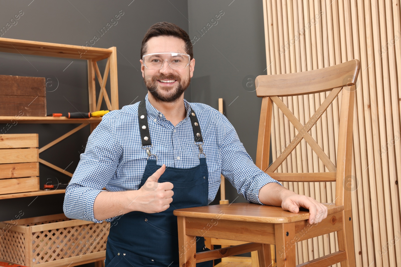 Photo of Relaxing hobby. Smiling man with wooden chair showing thumbs up in workshop