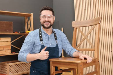 Relaxing hobby. Smiling man with wooden chair showing thumbs up in workshop