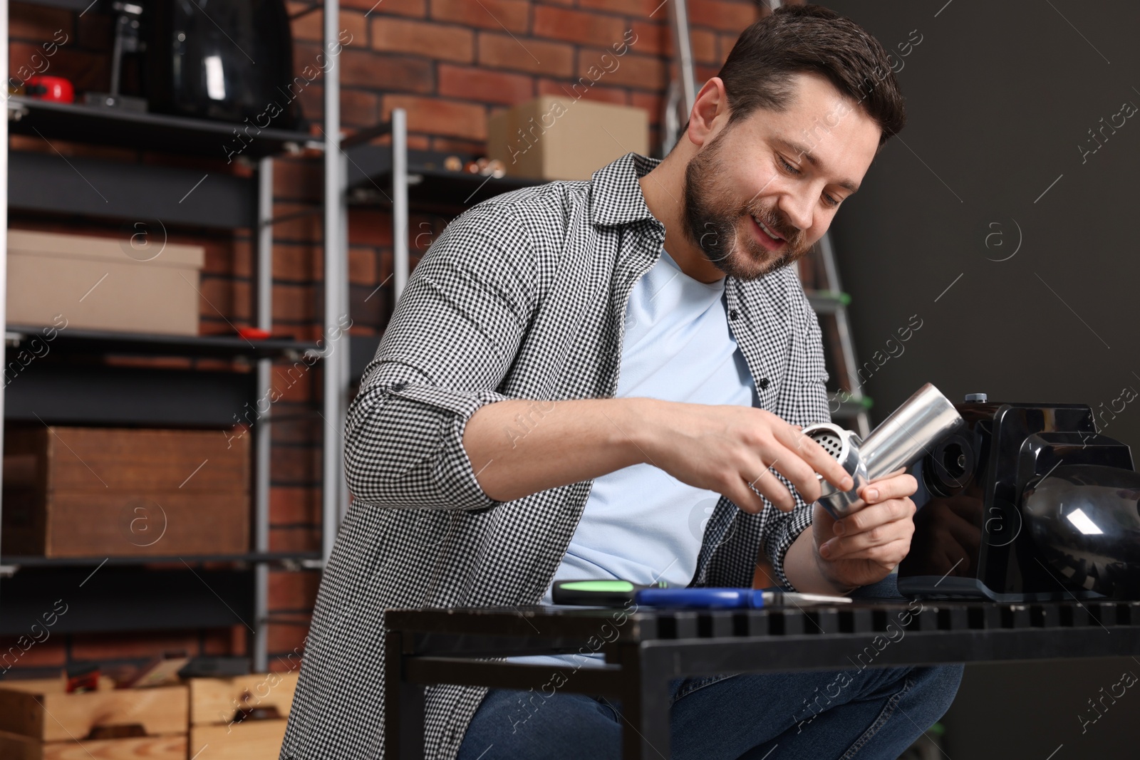 Photo of Relaxing hobby. Smiling man repairing electric meat grinder in workshop