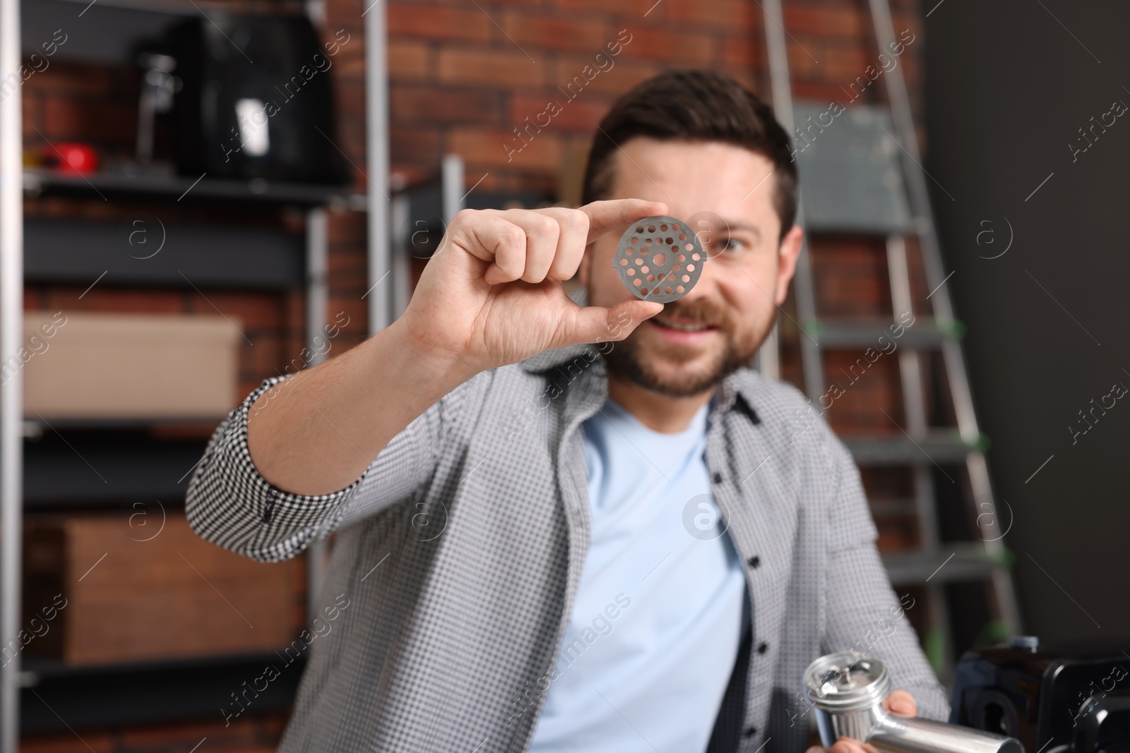 Photo of Relaxing hobby. Smiling man with part of electric meat grinder in workshop, selective focus