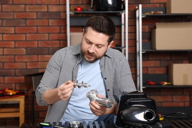 Photo of Relaxing hobby. Man examining parts of electric meat grinder in workshop