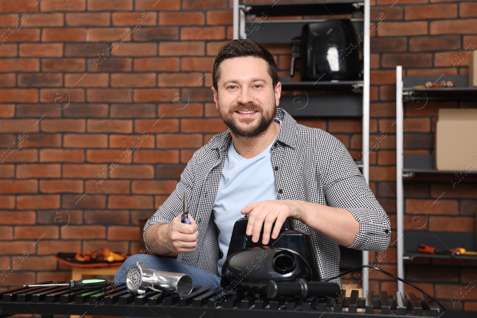 Photo of Relaxing hobby. Smiling man repairing electric meat grinder in workshop