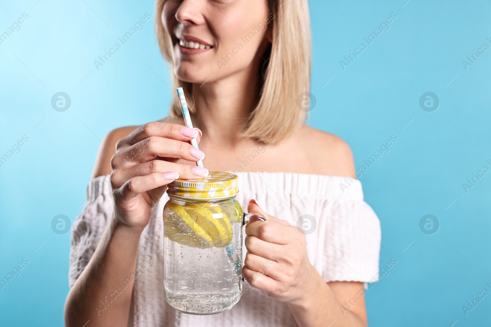 Photo of Woman with mason jar of lemonade on light blue background, closeup. Refreshing drink