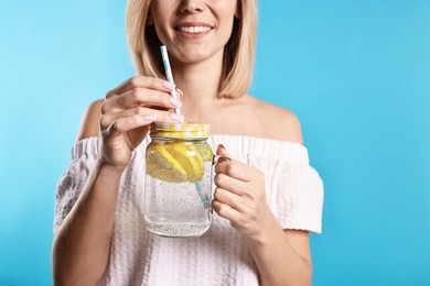 Photo of Woman with mason jar of lemonade on light blue background, closeup. Refreshing drink