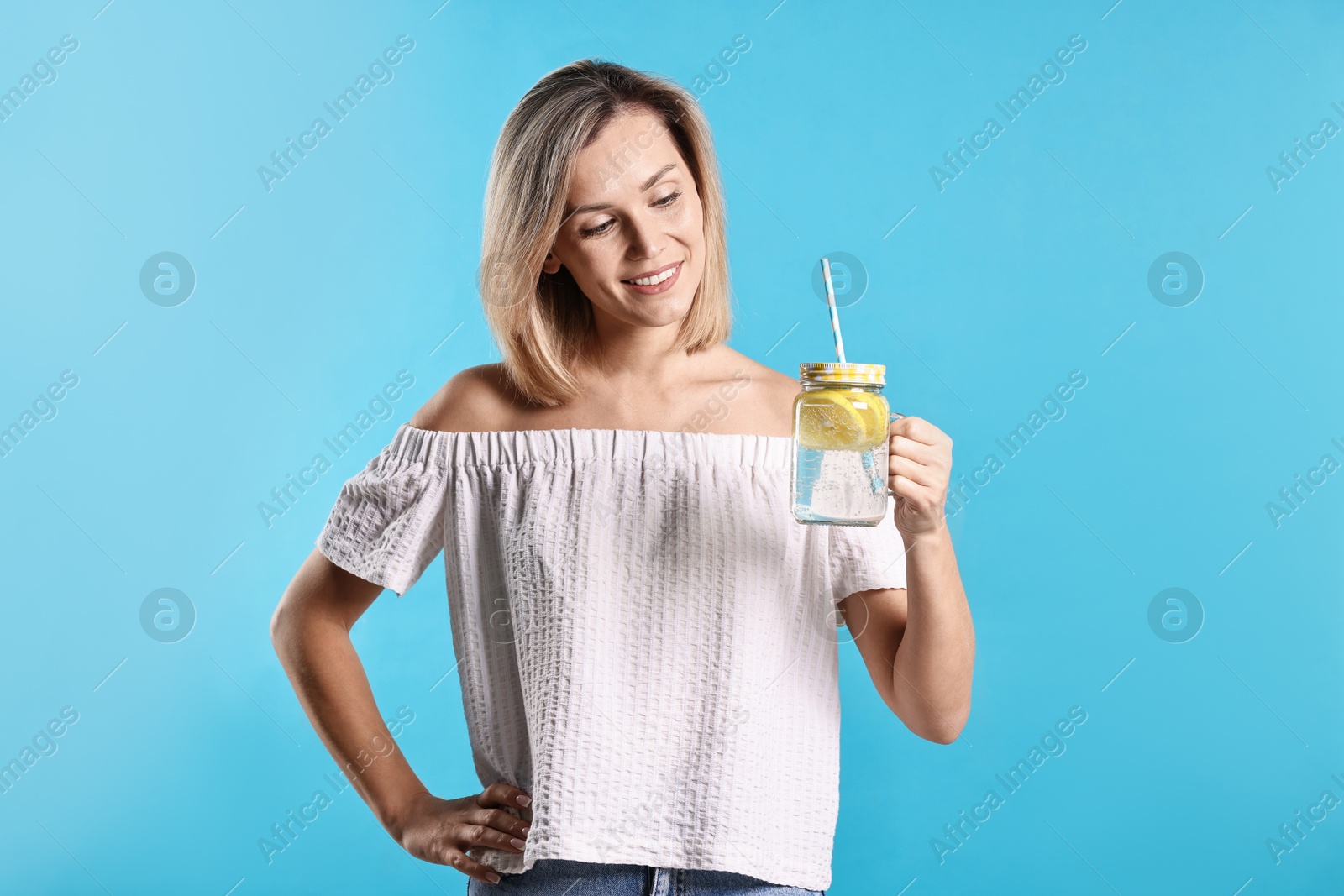 Photo of Woman with mason jar of lemonade on light blue background. Refreshing drink