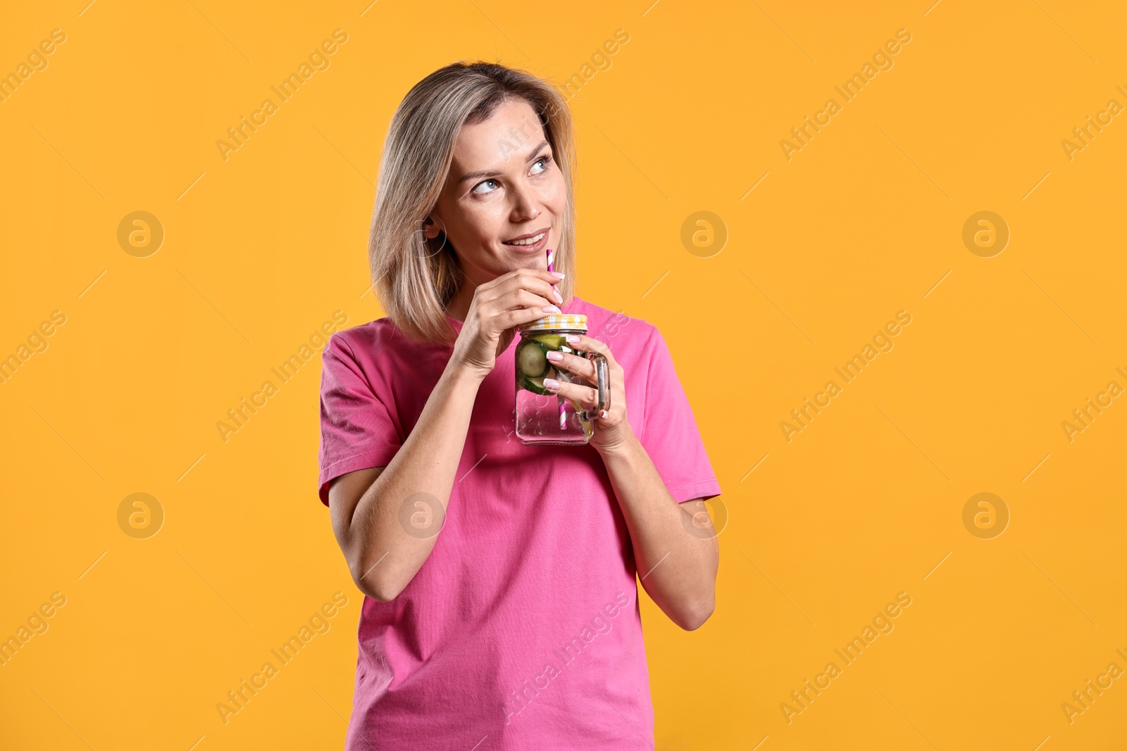 Photo of Woman drinking tasty cucumber water on orange background, space for text. Refreshing drink