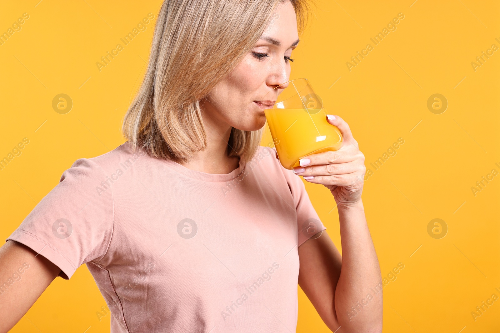 Photo of Woman drinking tasty juice on orange background. Refreshing drink