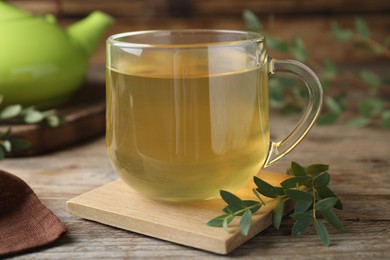 Photo of Glass cup of aromatic eucalyptus tea on wooden table, closeup