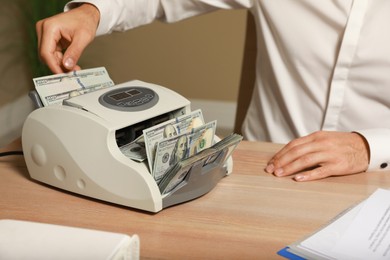 Photo of Man putting money into banknote counter at wooden table indoors, closeup