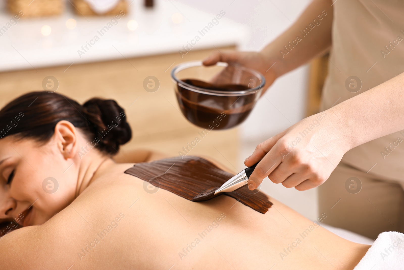 Photo of Chocolate body wrap. Spa worker applying mask onto woman's back in salon, closeup