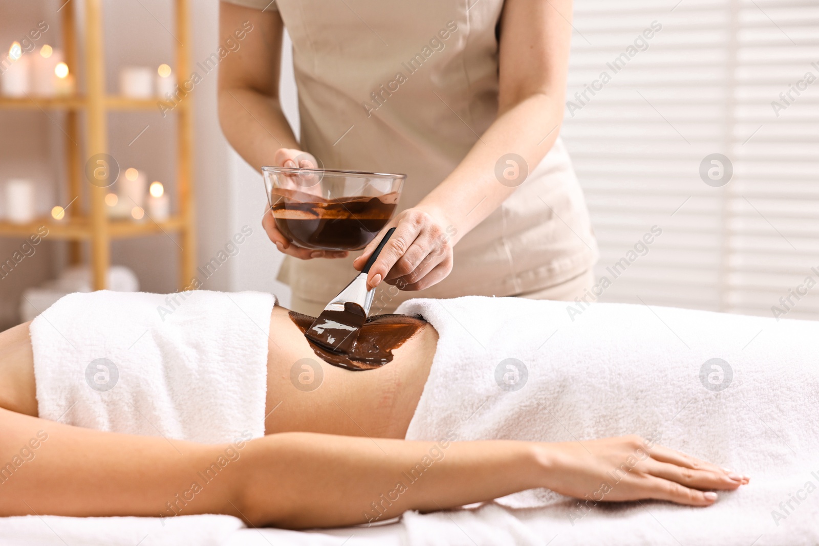 Photo of Chocolate body wrap. Spa worker applying mask onto woman's belly in salon, closeup