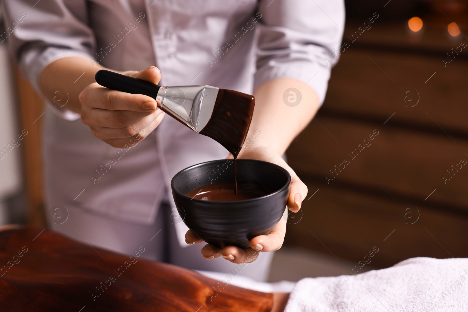 Photo of Spa worker with cosmetic product for chocolate body wrap near woman in salon, closeup. Space for text