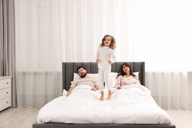 Photo of Happy playful daughter and her overwhelmed parents on bed at home