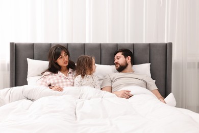 Photo of Happy playful daughter with her overwhelmed parents in bed at home