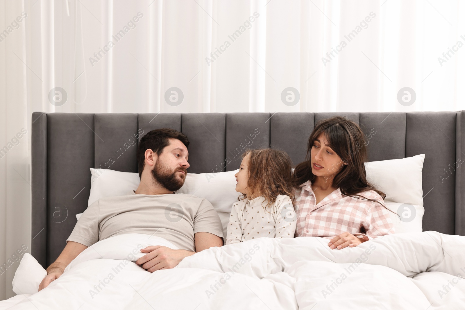 Photo of Playful daughter with her overwhelmed parents in bed at home