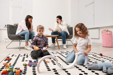 Photo of Hyperactive children playing while their overwhelmed parents talking at home