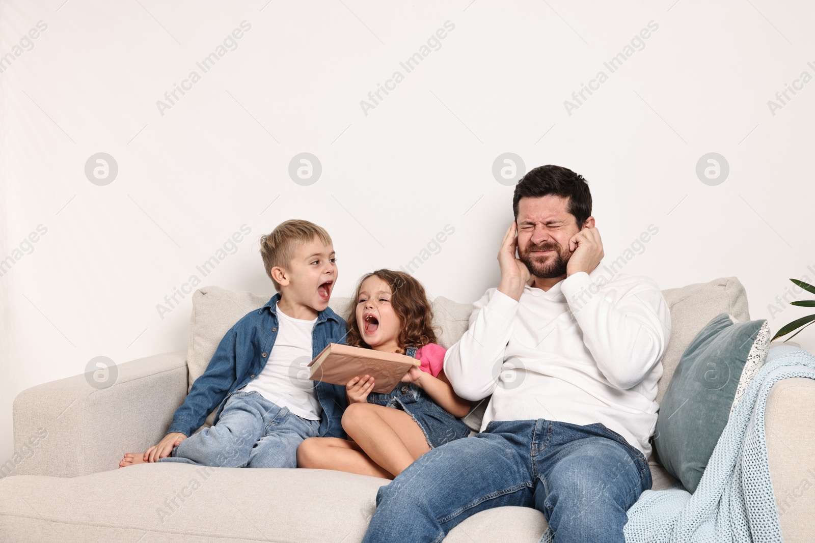 Photo of Overwhelmed father and his noisy children on sofa at home