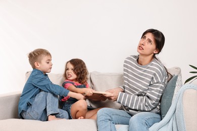 Photo of Overwhelmed mother and her naughty children with book on sofa at home