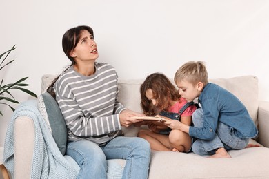 Photo of Overwhelmed mother and her naughty children with book on sofa at home