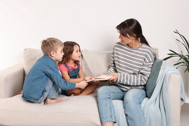 Photo of Overwhelmed mother and her naughty children with book on sofa at home