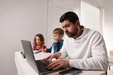 Photo of Naughty children and their overwhelmed father at table with laptop indoors