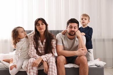 Photo of Playful children and their overwhelmed parents on bed at home