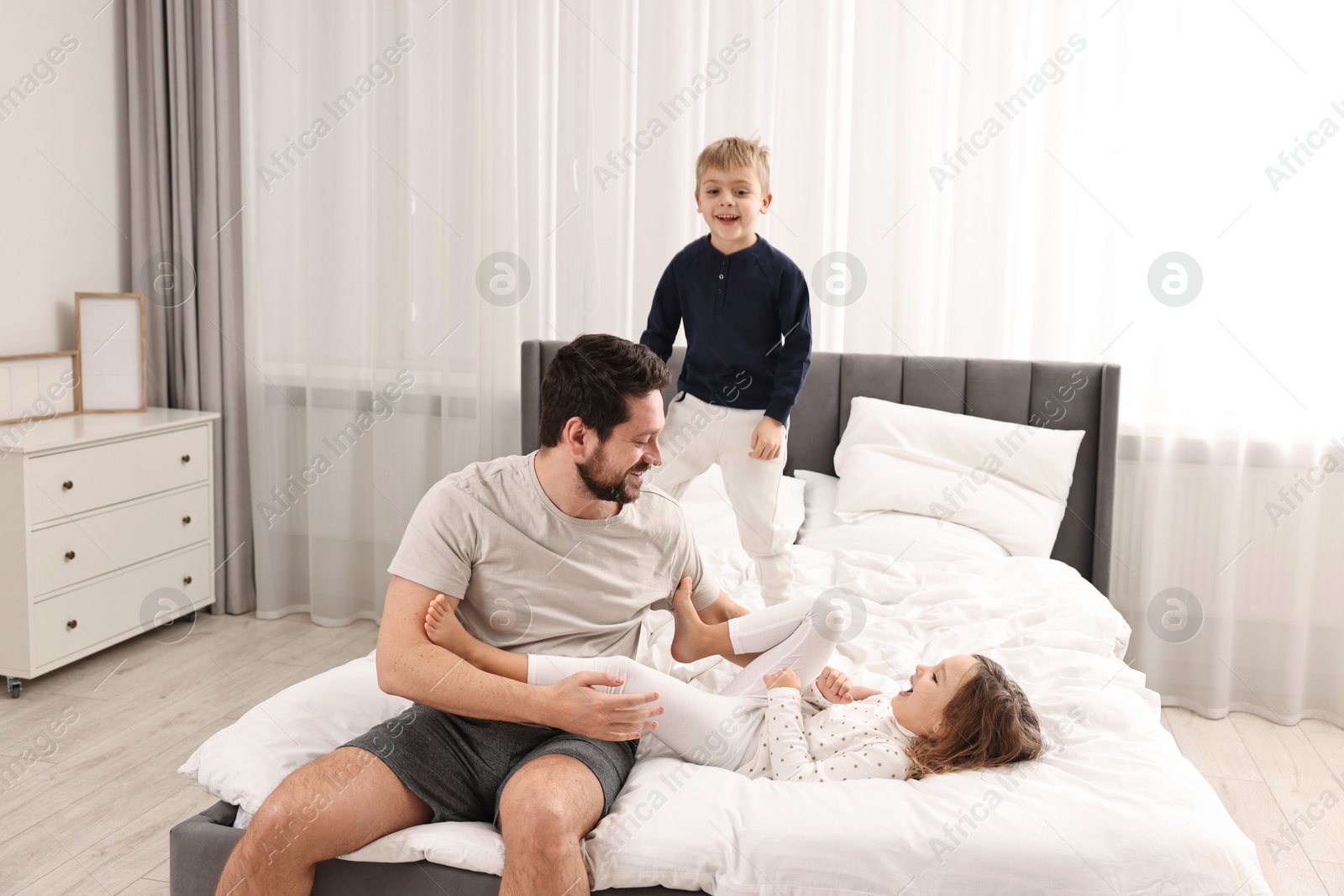 Photo of Happy father playing with his children on bed at home