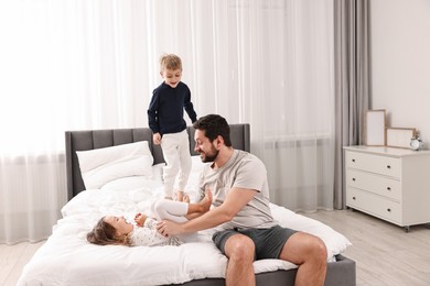 Photo of Happy father playing with his children on bed at home