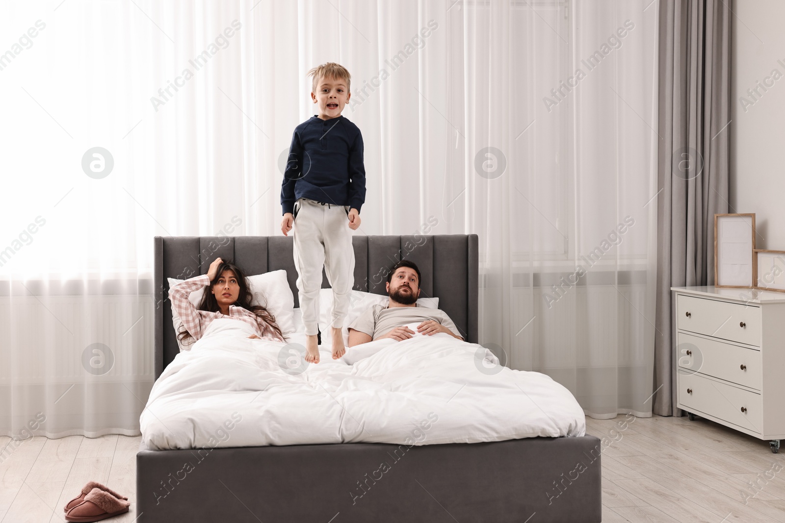 Photo of Overwhelmed parents and their playful son on bed at home