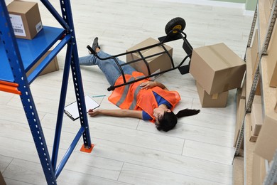 Photo of Accident at work. Unconscious woman and overturned hand truck on floor in warehouse