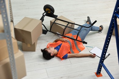 Photo of Accident at work. Unconscious woman and overturned hand truck on floor in warehouse