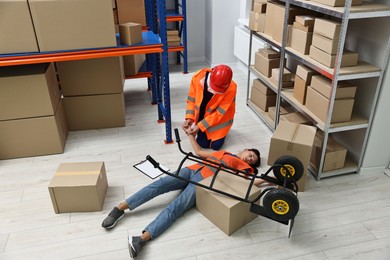 Photo of Accident at work. Man checking pulse of his unconscious colleague in warehouse