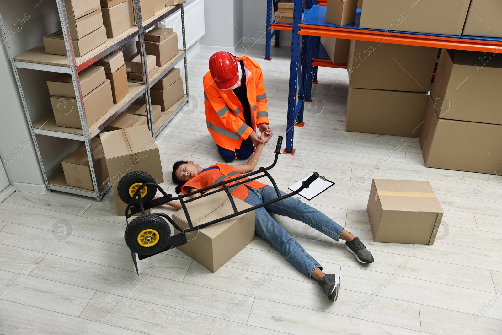 Photo of Accident at work. Man checking pulse of his unconscious colleague in warehouse