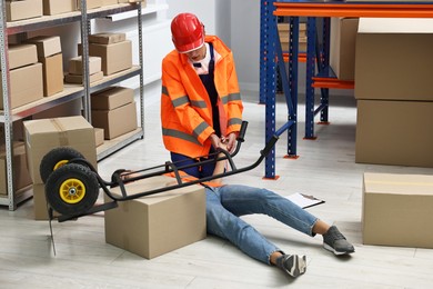 Photo of Accident at work. Man checking pulse of his unconscious colleague in warehouse