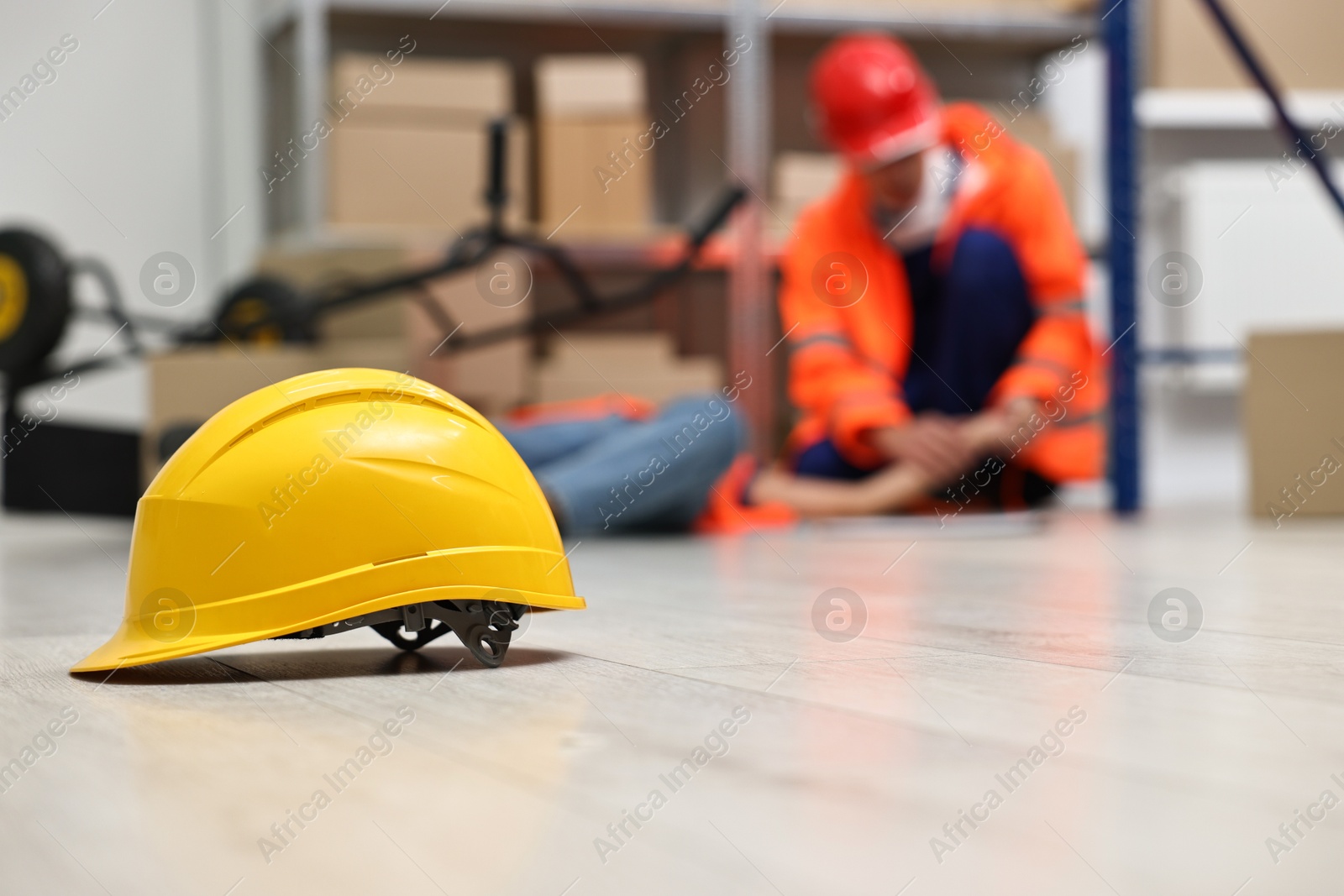 Photo of Accident at work. Hardhat on floor and man helping his injured colleague in warehouse, selective focus