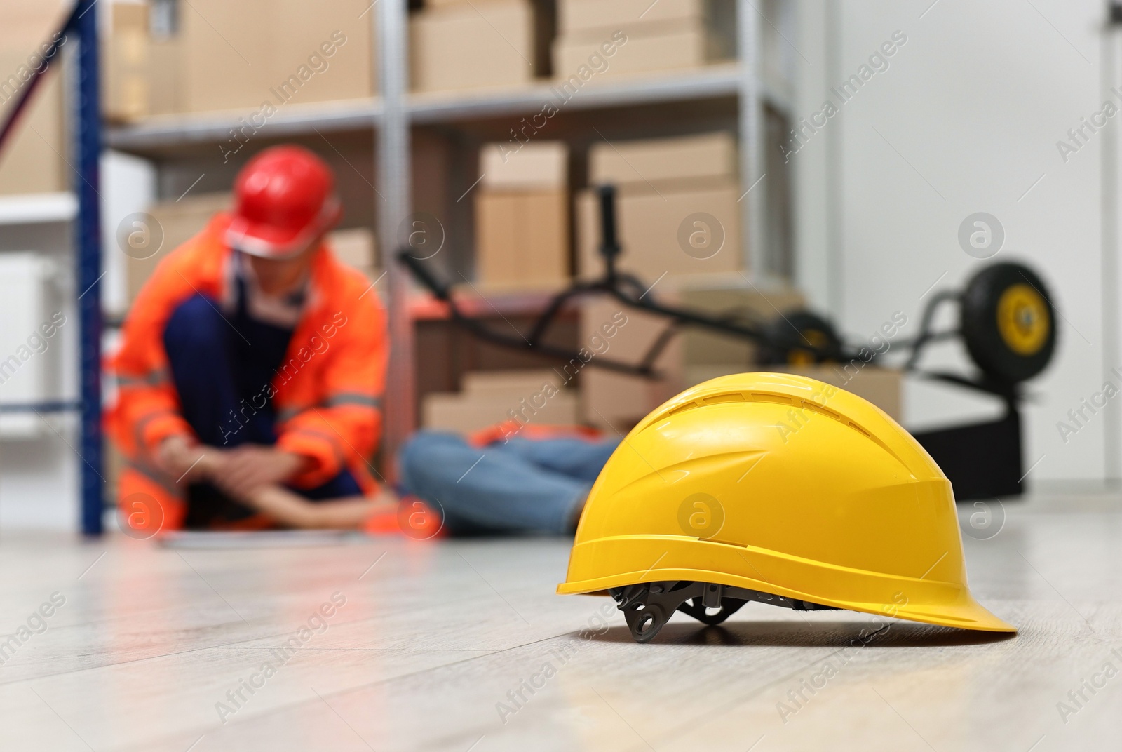 Photo of Accident at work. Hardhat on floor and man helping his injured colleague in warehouse, selective focus