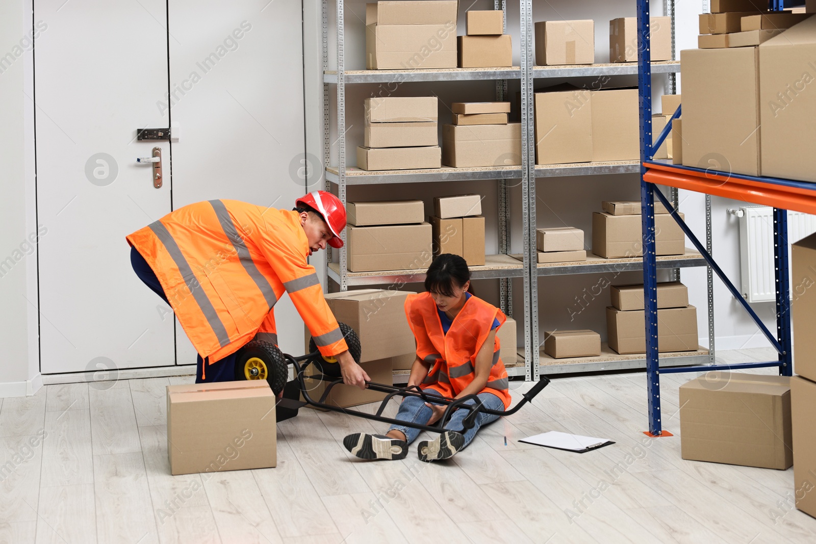 Photo of Accident at work. Man helping his injured colleague in warehouse