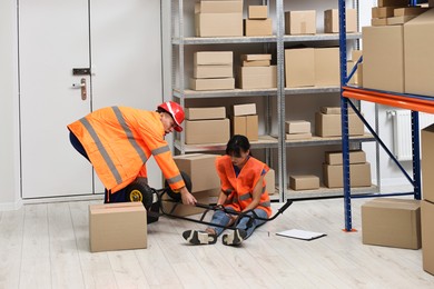 Photo of Accident at work. Man helping his injured colleague in warehouse