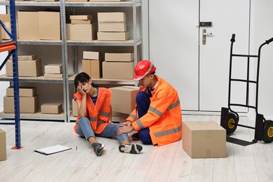 Photo of Accident at work. Man helping his injured colleague in warehouse