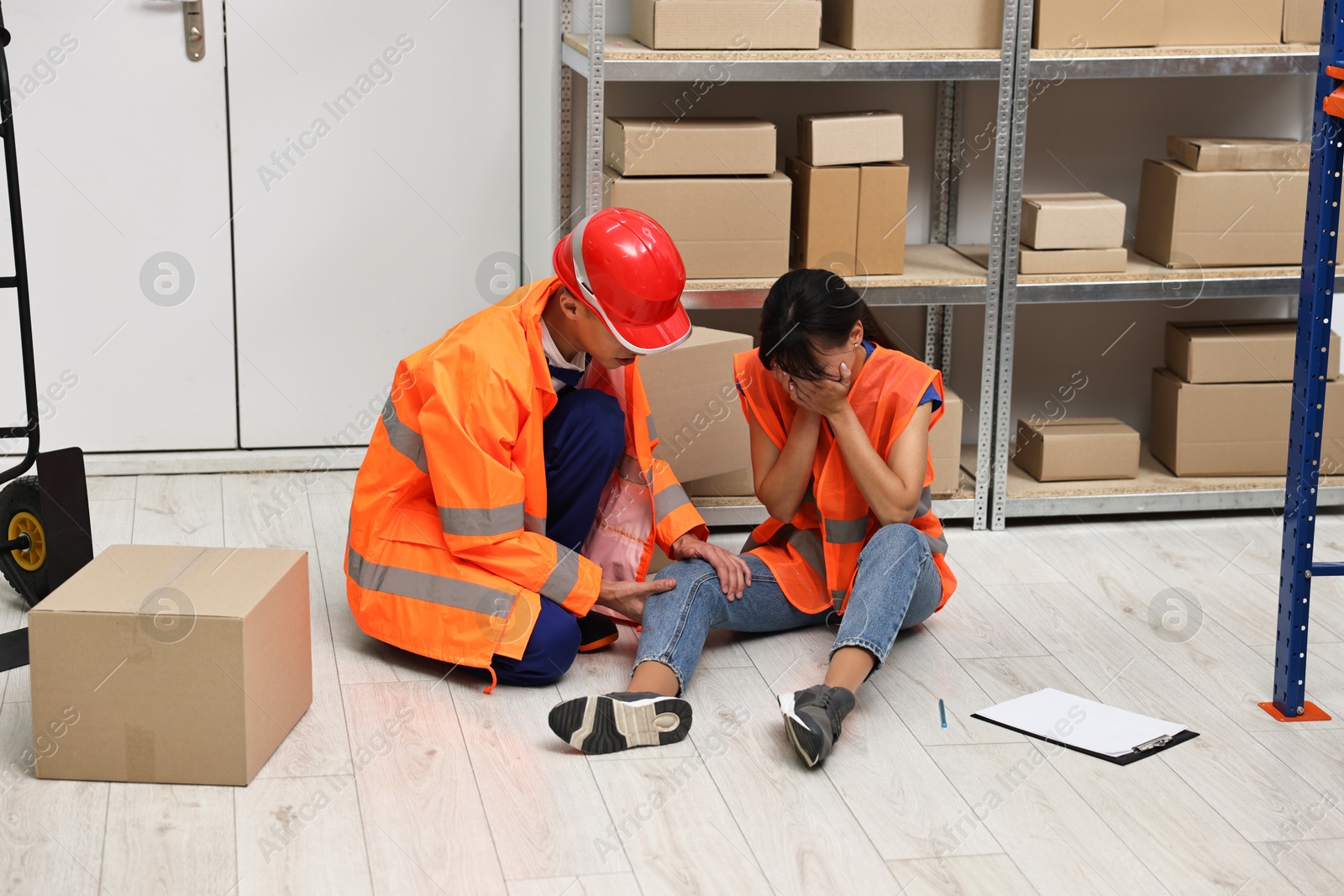 Photo of Accident at work. Man helping his injured colleague in warehouse