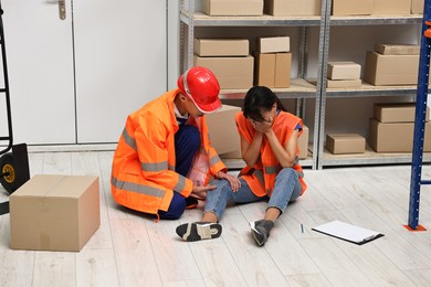 Photo of Accident at work. Man helping his injured colleague in warehouse