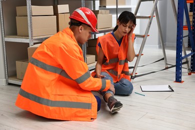 Photo of Accident at work. Man helping his injured colleague in warehouse