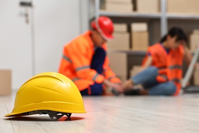 Photo of Accident at work. Hardhat on floor and man helping his injured colleague in warehouse, selective focus